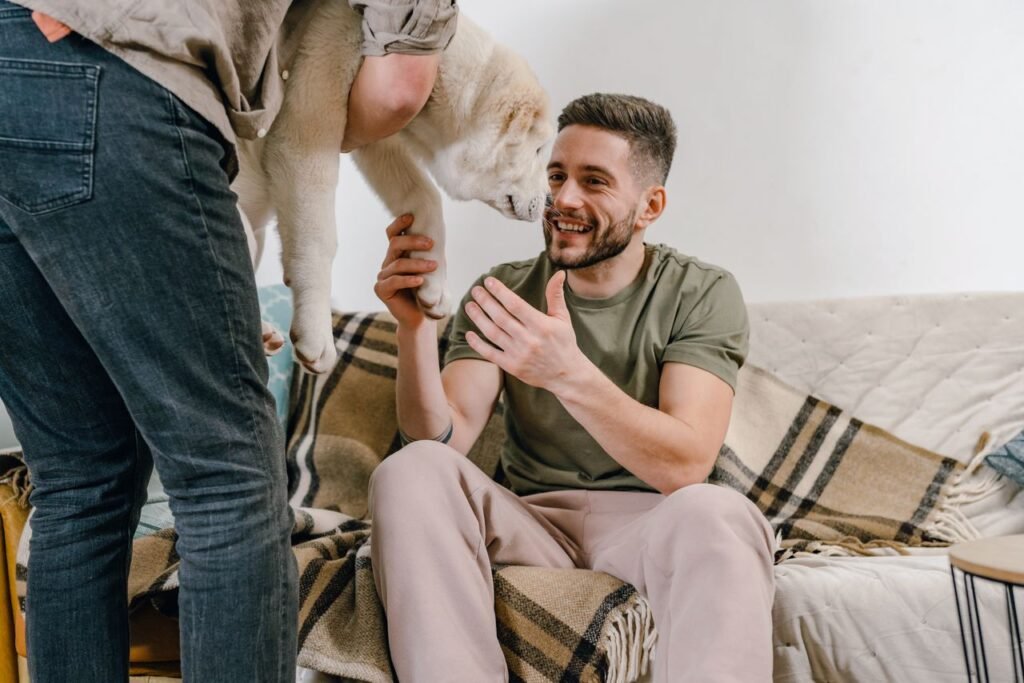 A smiling man playing with a dog indoors, showcasing a joyful moment on a cozy sofa.